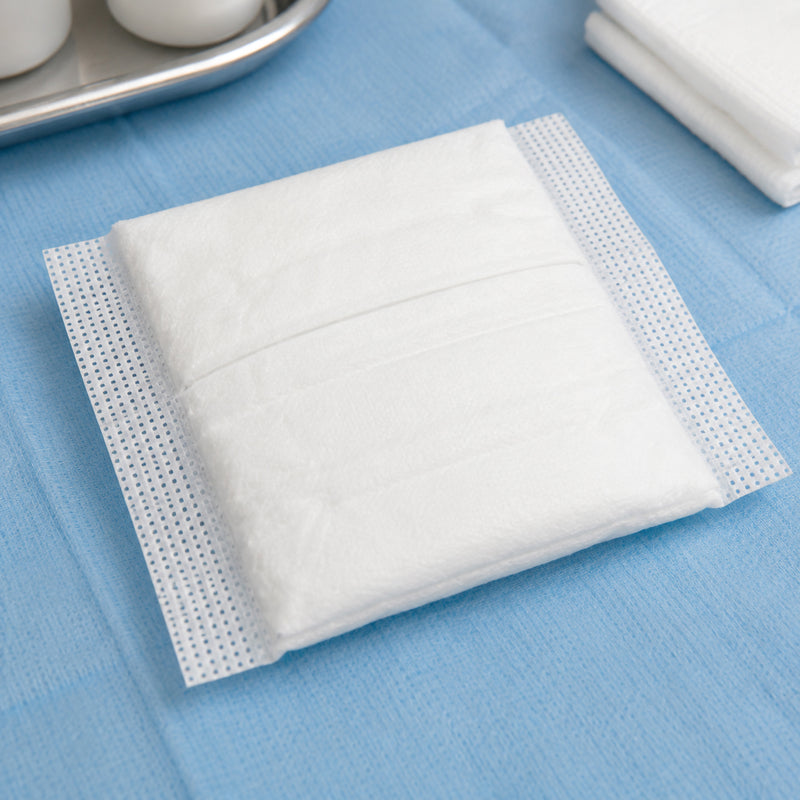 Close view of a white AeroWound Combine Dressing resting on a blue clinical surface. The image clearly shows the soft absorbent square pad and textured side sections, providing customers with a detailed view of the dressing construction and compact 10 x 10cm format used for absorbent wound protection.