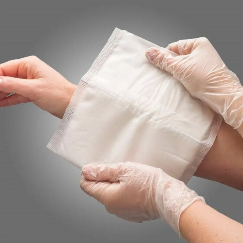 Gloved healthcare professional positioning a large AeroWound Combine Dressing around a persons wrist and forearm. The image highlights the flexible 20 x 20cm format and substantial padded coverage, demonstrating how the dressing can conform around a limb while providing a broad absorbent layer for wound care.