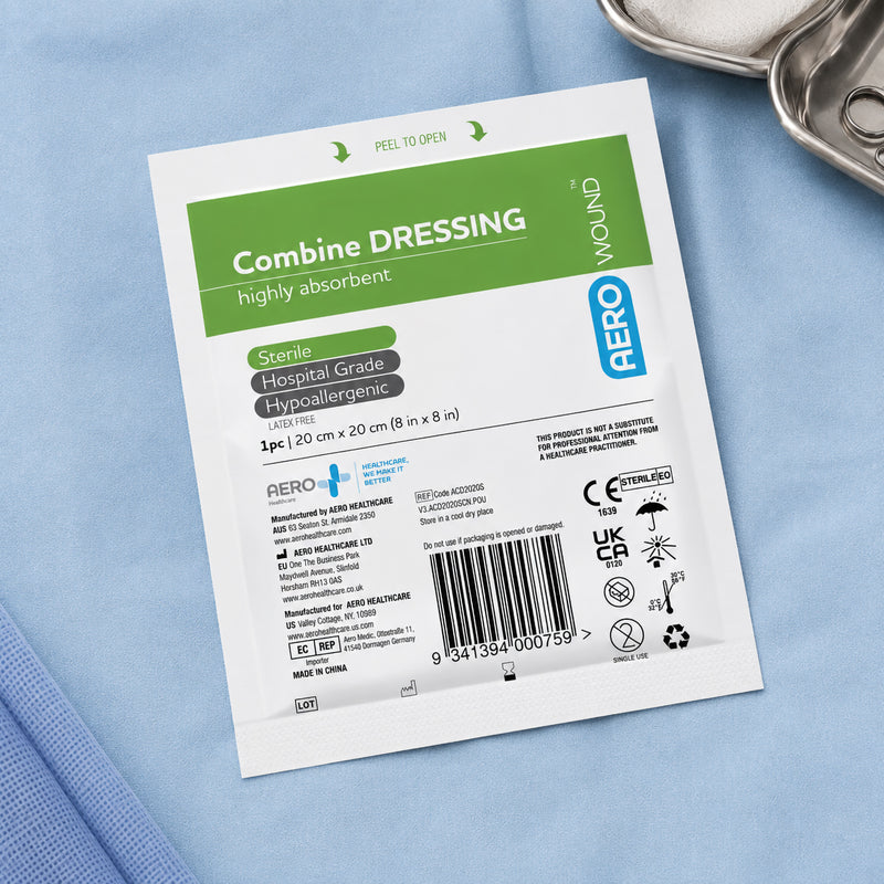 Individually packaged AeroWound Combine Dressing presented on a blue clinical surface beside wound care instruments. The sterile pouch identifies the dressing as highly absorbent, hospital grade, hypoallergenic and latex free, with the 20 x 20cm size clearly displayed for convenient identification before treatment.