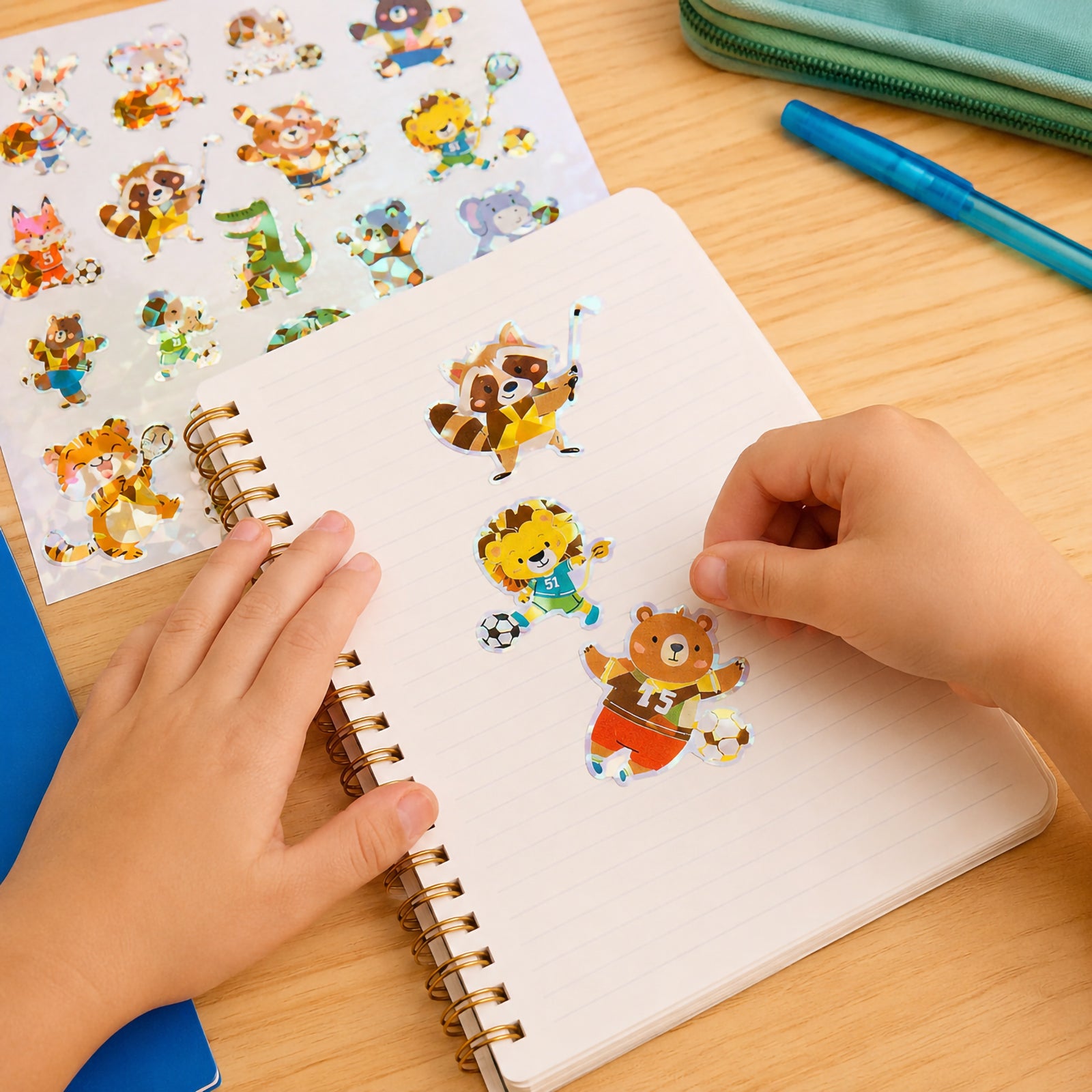 Child decorating a notebook with holographic animal athlete stickers featuring a raccoon hockey player, lion soccer player and bear football character. The sparkling foil designs encourage creative play and personalisation.