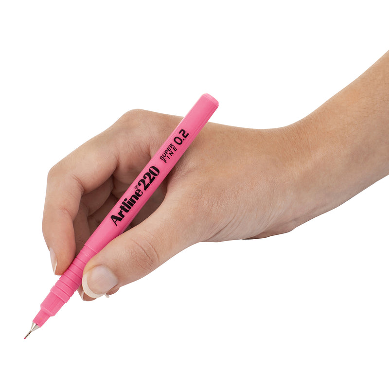 A close up of a hand holding the Artline 220 Fineliner Pen 0.2mm Pink against a white background, clearly showing the ergonomic grip, slim plastic barrel and ultra fine metal supported tip designed for accurate writing, technical drawing and fine detail illustration.