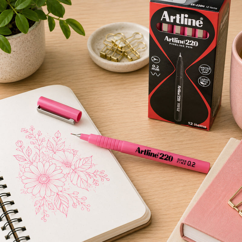An uncapped Artline 220 Fineliner Pen 0.2mm Pink is displayed beside its retail box on a tidy desktop with a sketchbook featuring intricate floral line art. The scene highlights the precision tip, premium packaging and suitability for illustration, technical drawing, journalling and detailed creative work.