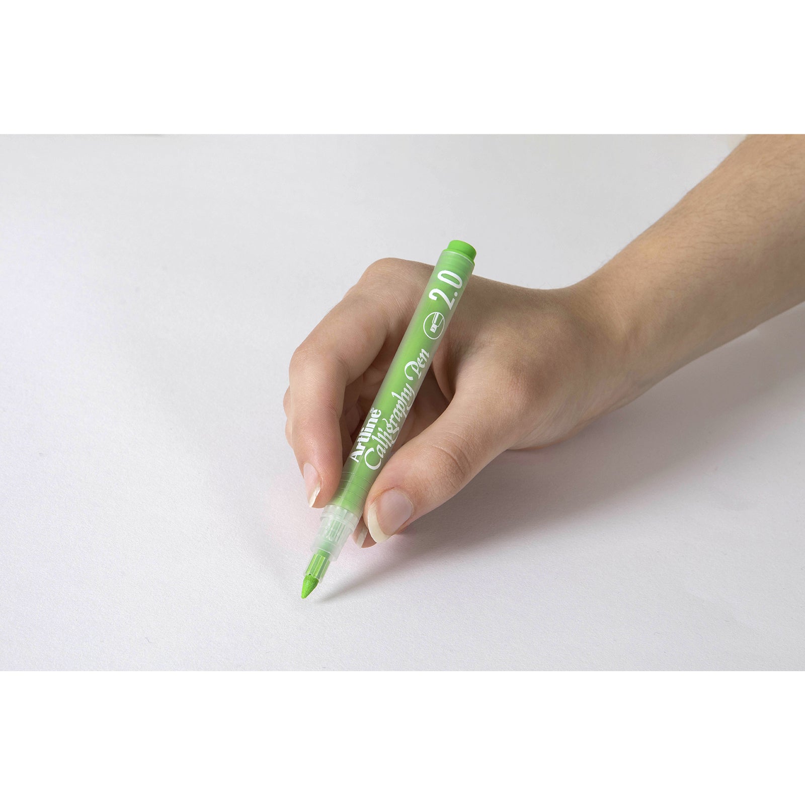 A close up of a hand holding the Artline Calligraphy Pen 2.0mm Pastel Lime Green against a clean white background, highlighting the comfortable grip, translucent barrel and broad calligraphy nib for accurate lettering and decorative writing.