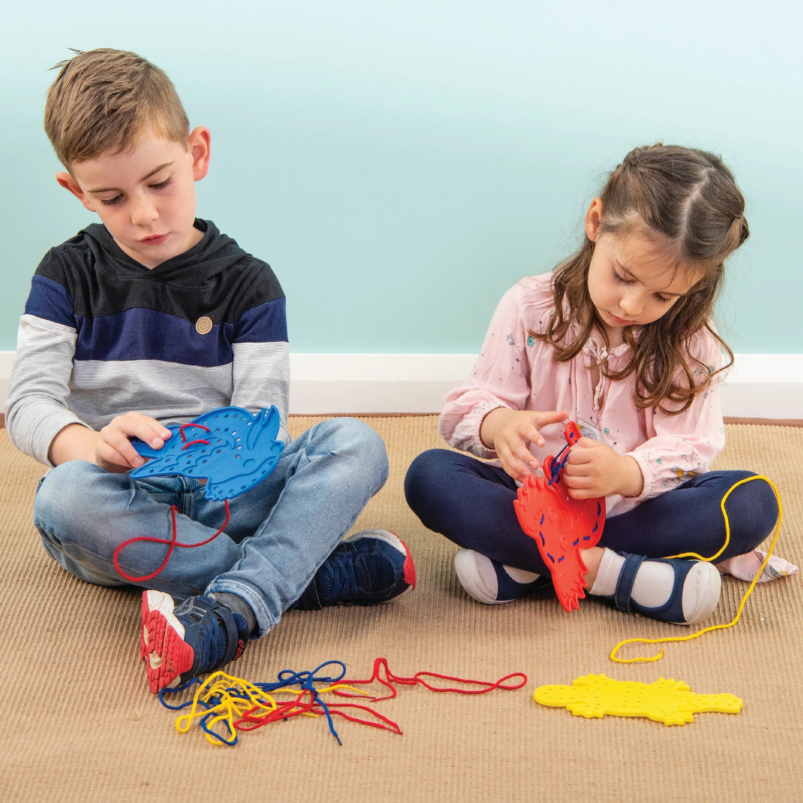 Young children engaged in fine motor learning activities using Educational Colours Australian animal lacing boards with colourful cords spread across the floor during interactive play.