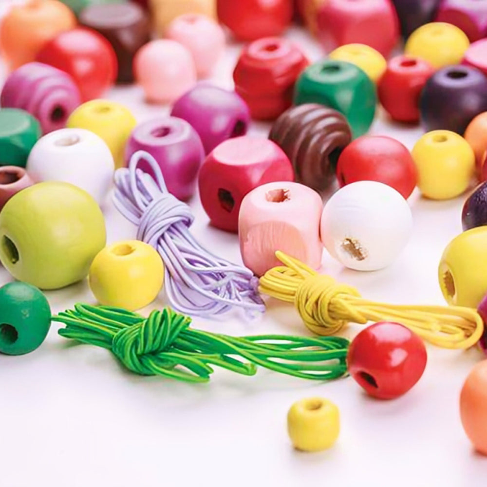 Colourful assortment of wooden craft beads in multiple shapes and sizes displayed with green, yellow, and purple threading cords on a white background, ideal for jewellery making and educational threading activities.