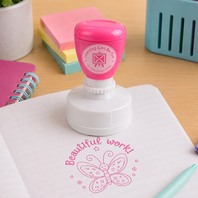 Self inking reward stamp shown with educational supplies and pastel stationery. The vibrant pink butterfly impression highlights creative accomplishments and encourages students to take pride in their work.