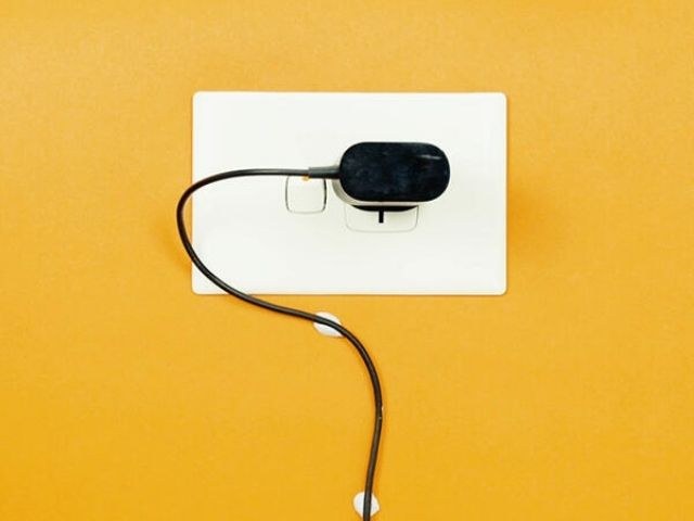 Phone charger cable held neatly to a white wall plate with small pieces of blue Blu Tack on a yellow wall
