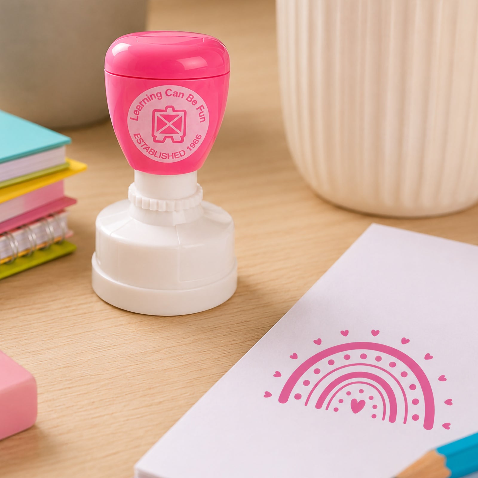 Bright Thinking merit stamp positioned near study materials and classroom supplies. The bold pink rainbow design creates positive feedback for learners while encouraging confidence, participation and academic success.