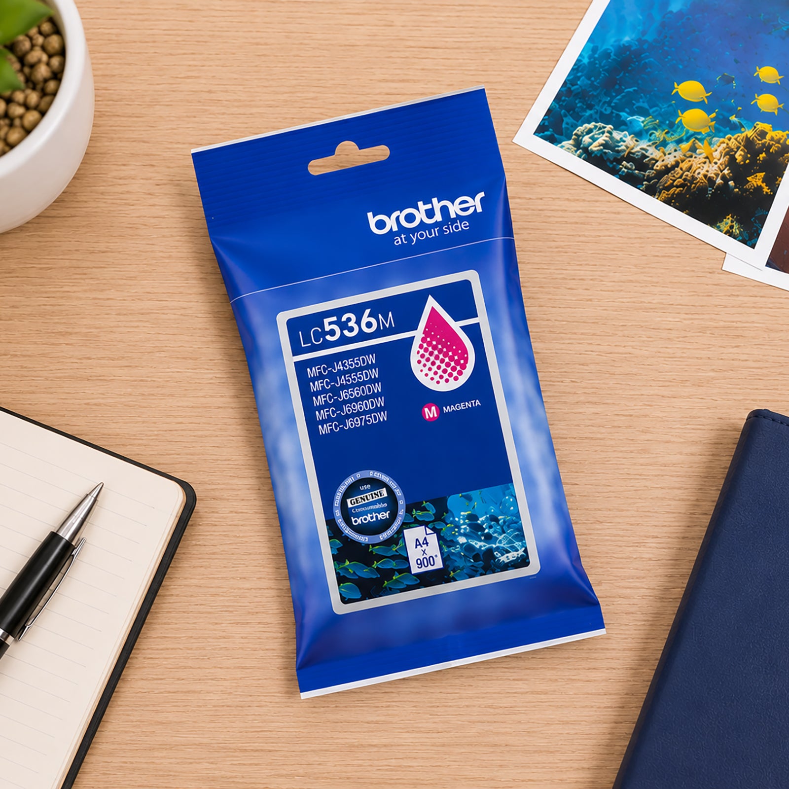 Top down desktop scene featuring the Brother LC536M Magenta Ink Cartridge alongside notebooks, office accessories and colourful printed photographs. The image showcases the cartridge's suitability for creative projects, photo printing and high quality colour document production.