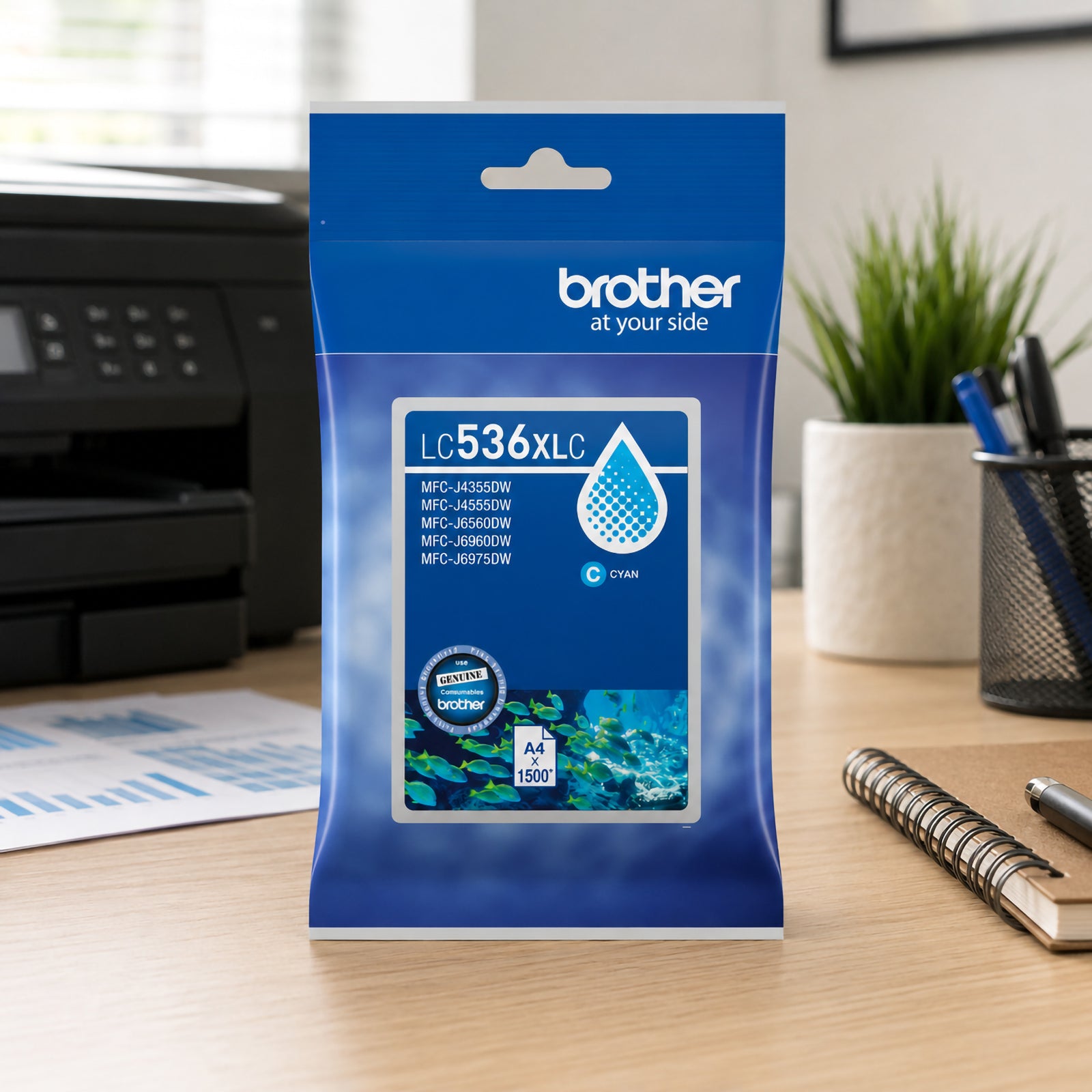 Brother LC536XLC High Yield Cyan Ink Cartridge displayed on a modern office desk beside a Brother multifunction printer. The cartridge packaging stands upright near a notebook, coffee cup and printed photo documents, creating a productive workspace setting. The image emphasises reliable colour printing performance for home offices, creative projects and everyday business document production.