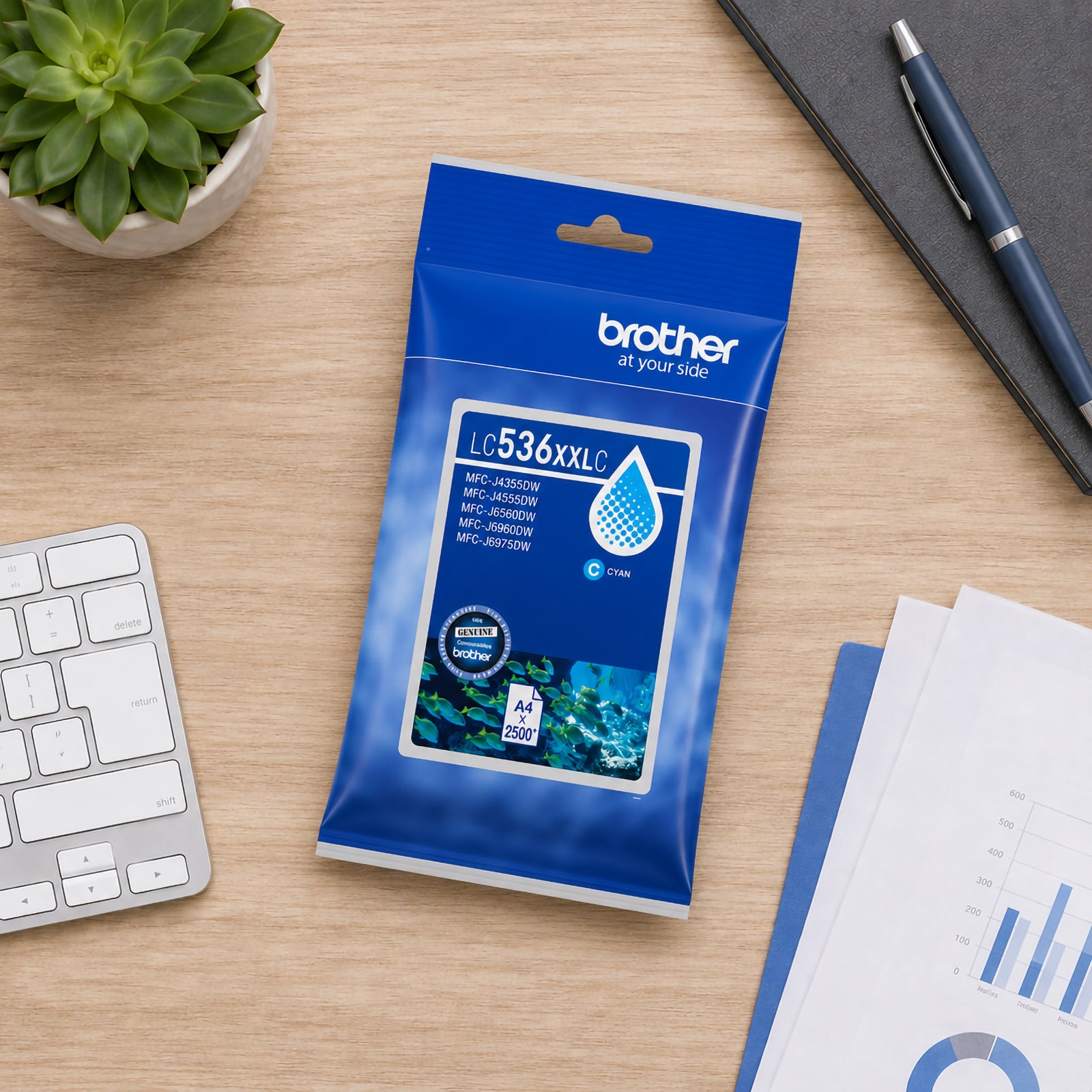 Top down workspace view featuring the Brother LC536XXLC cyan ink cartridge package positioned on a timber desk alongside a keyboard, business documents, notebook and desktop plant. The image showcases a productive office setting focused on efficient, high quality colour printing.