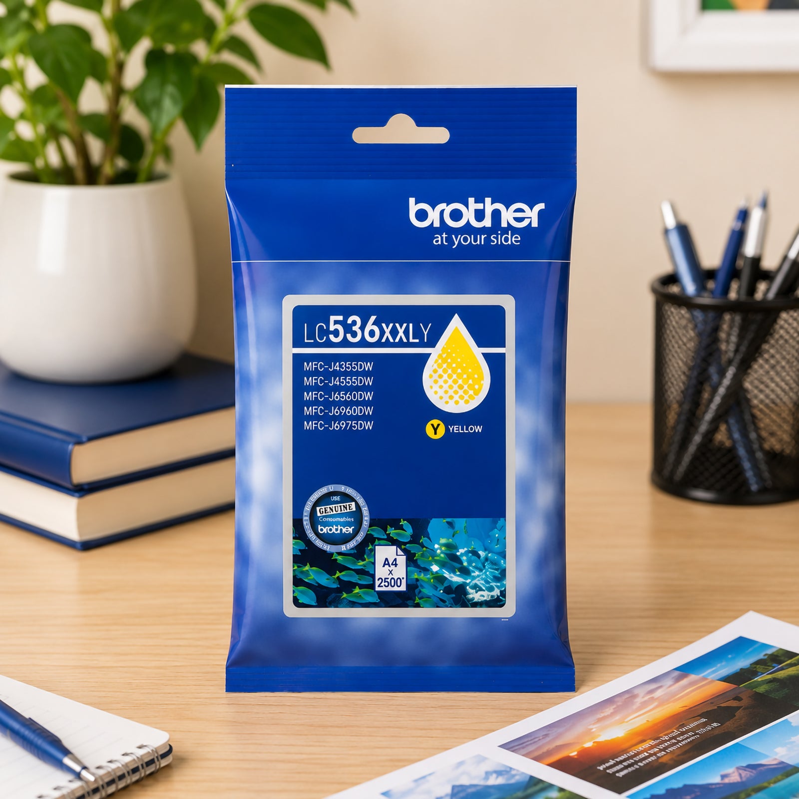 Front facing display of the Brother LC536XXLY super high yield yellow ink cartridge package positioned on a tidy office desk with stationery, printed documents and indoor plants. The image emphasises professional printing quality and high yield performance for business users.