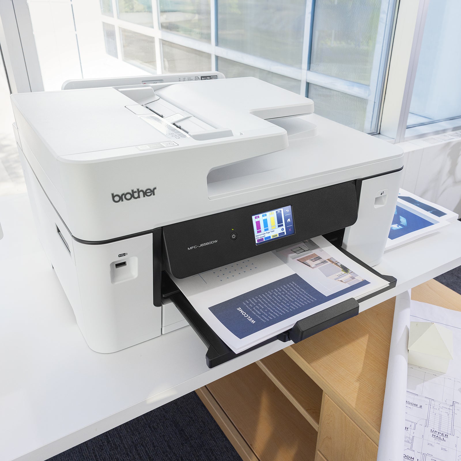 Close angle view of the Brother MFC J6560DW A3 printer actively producing a professional colour brochure. The touchscreen display and automatic document feeder are visible, demonstrating easy operation and efficient document handling for busy workgroups.