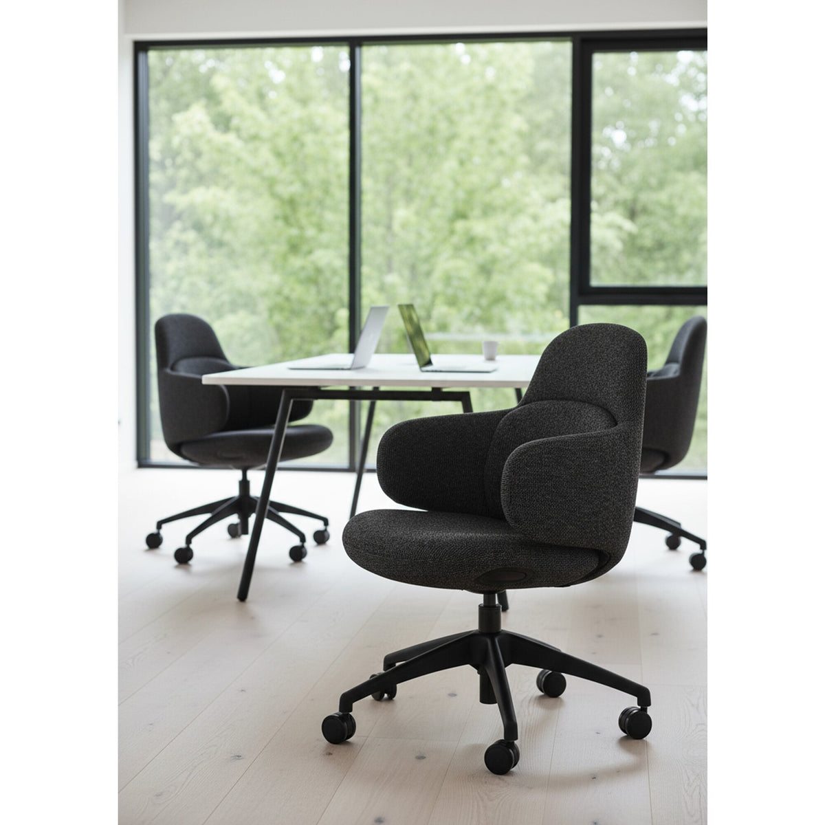 Dark grey Buro Odyssey chairs around a white round table beside tall windows in a bright meeting space