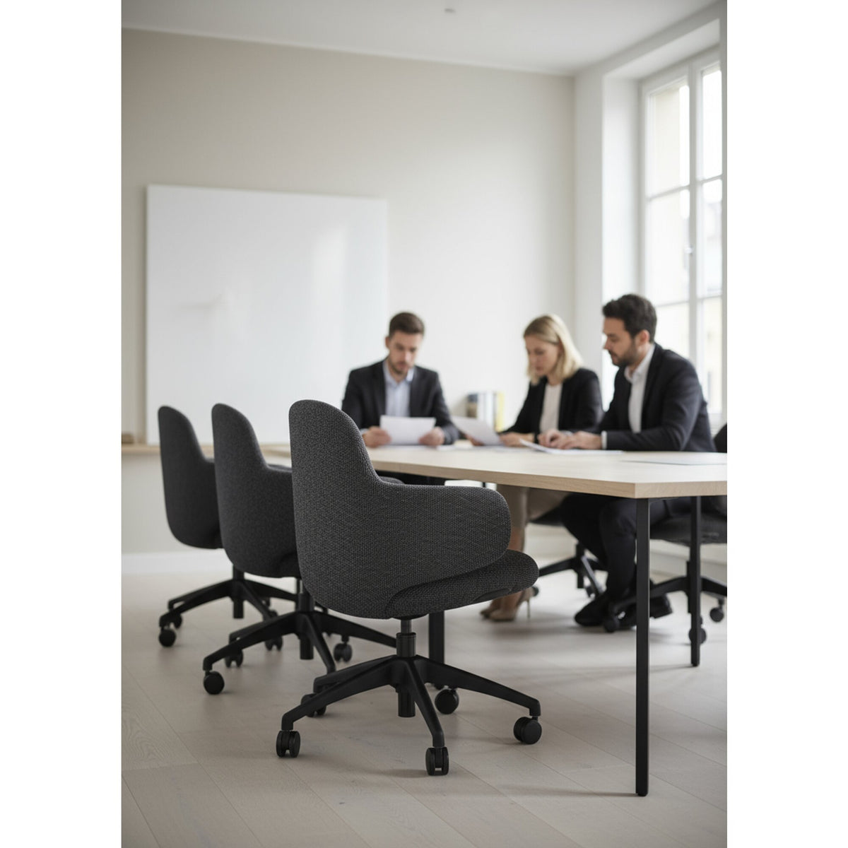Three people working at a long meeting table seated in dark grey Buro Odyssey chairs on black castor bases