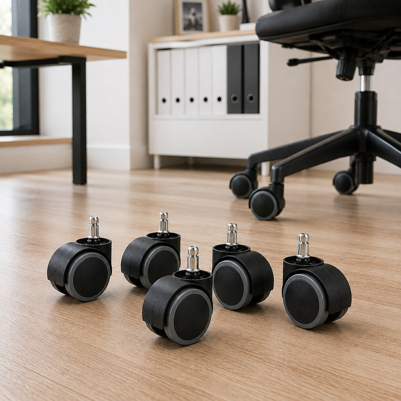 Five Buro Soft PU 60mm office chair castors arranged on a timber floor in a modern workspace, showing black castor housings, grey polyurethane wheel surfaces and silver mounting stems with an office chair behind.