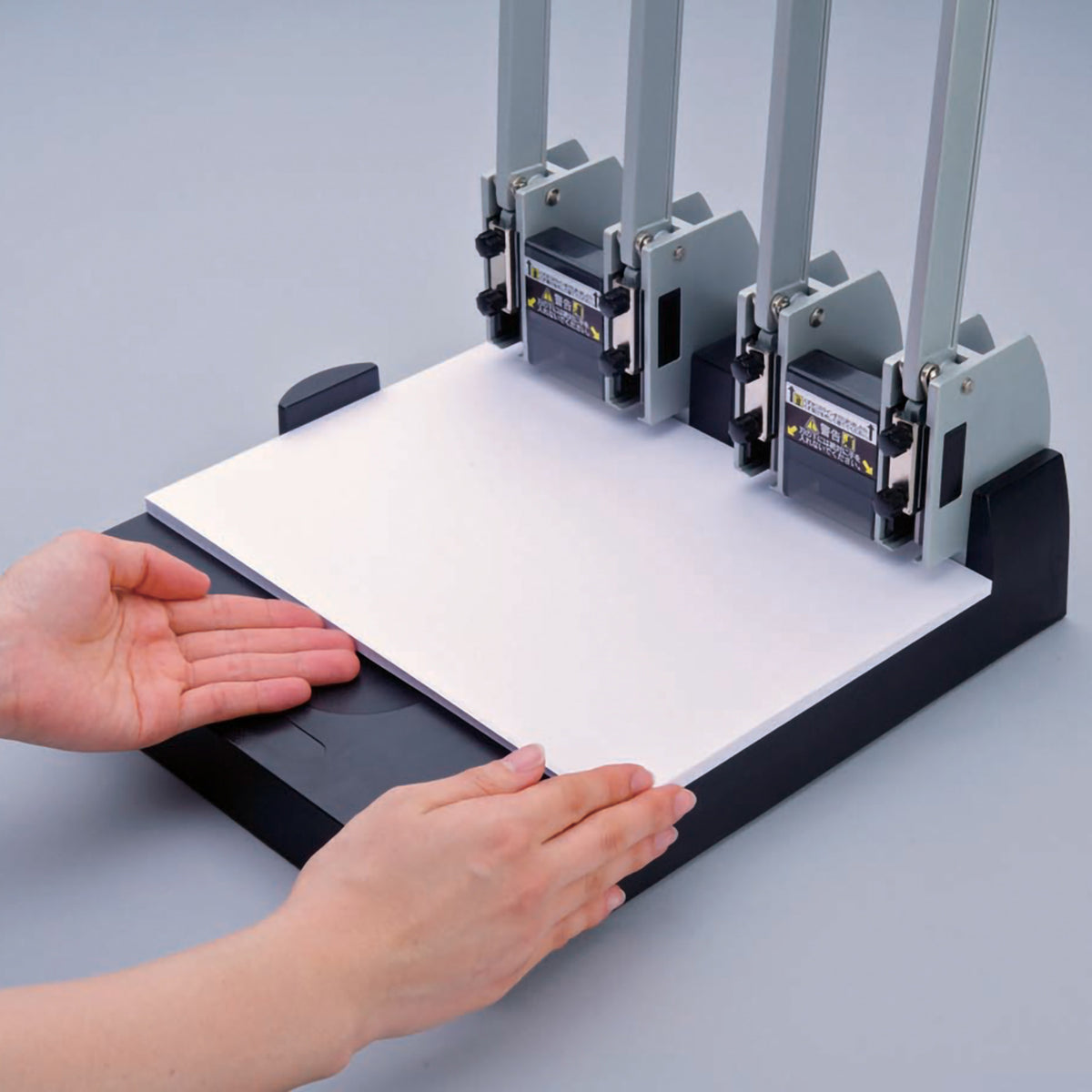 Two hands squaring a thick stack of white paper against the guide on the base of the four head punch