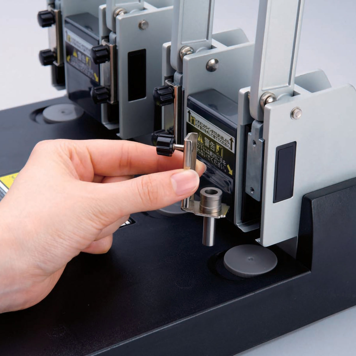 Fingers fitting a hollow punching blade into one of the punch heads of the Carl 124N