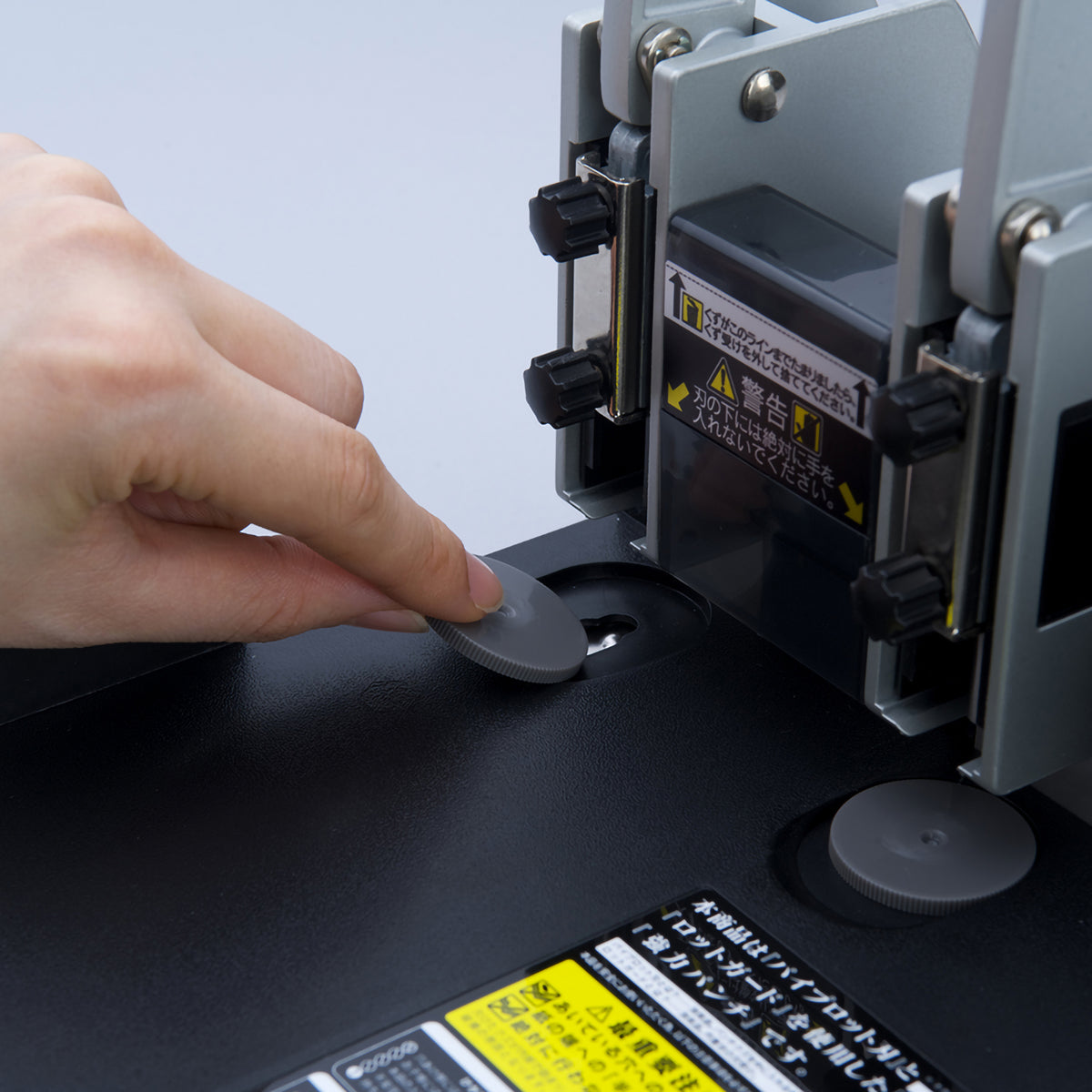 Finger pressing a grey support disc into its socket in the base under a punch head