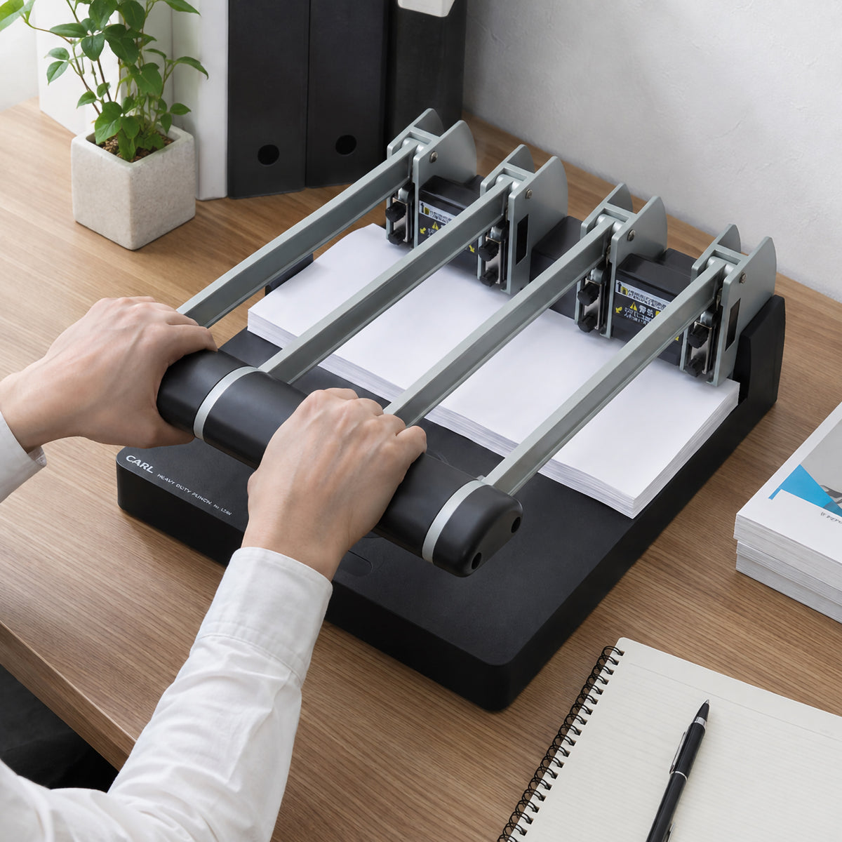 Store image: two hands pressing down the handle bar of a Carl punch on a wooden desk