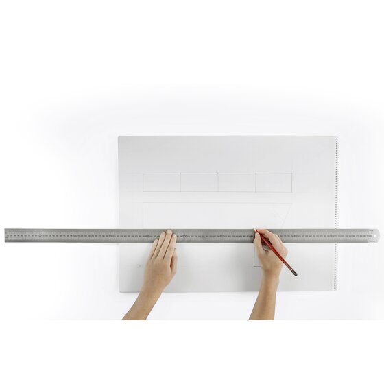 Two hands holding a Celco metre length stainless steel ruler across a large sheet of paper while ruling a pencil line