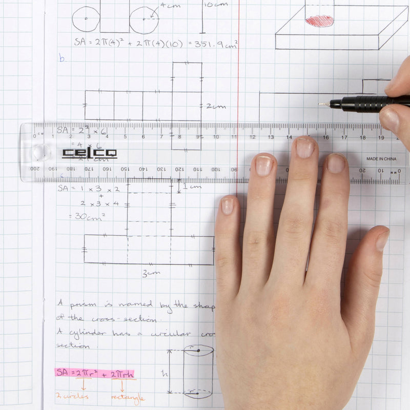 A close up overhead view shows the Celco 20cm clear ruler being used on graph paper while drawing technical mathematics diagrams. One hand steadies the ruler while another draws a straight line, demonstrating precise measuring and drafting.