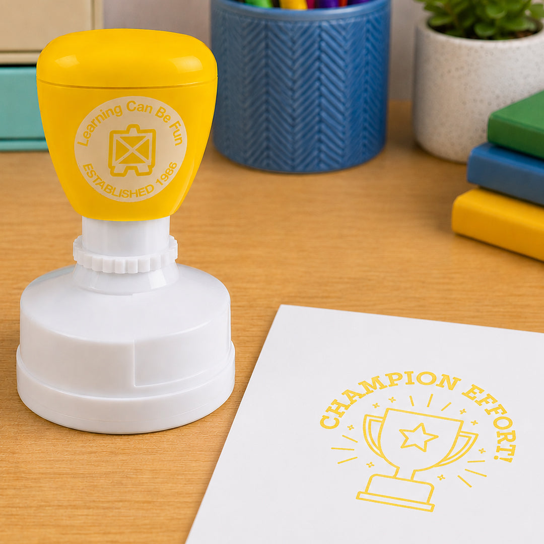 Self inking reward stamp shown in a learning environment with books and stationery. The trophy themed impression highlights effort, resilience and commitment to improvement across classroom activities.
