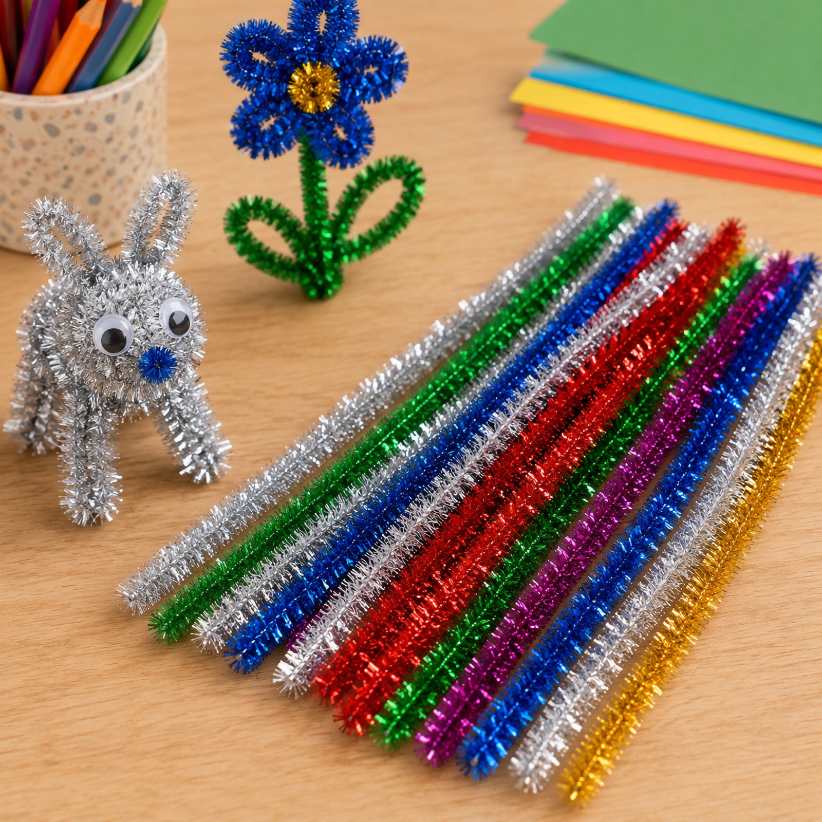 Close up of assorted tinsel chenille stems in bright metallic colours displayed beside a crafted rabbit and flower. The image highlights the shimmering texture, flexible construction and creative possibilities for sculpture, animal making and decorative craft projects.