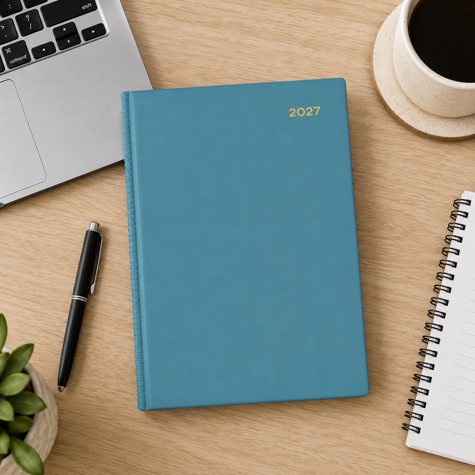 Top view of the Collins Belmont Colours 2027 A5 Day to a Page Teal Diary placed on a timber desk beside a laptop, coffee cup, notebook, pen and indoor plant. The calming teal cover creates a clean and organised workspace.