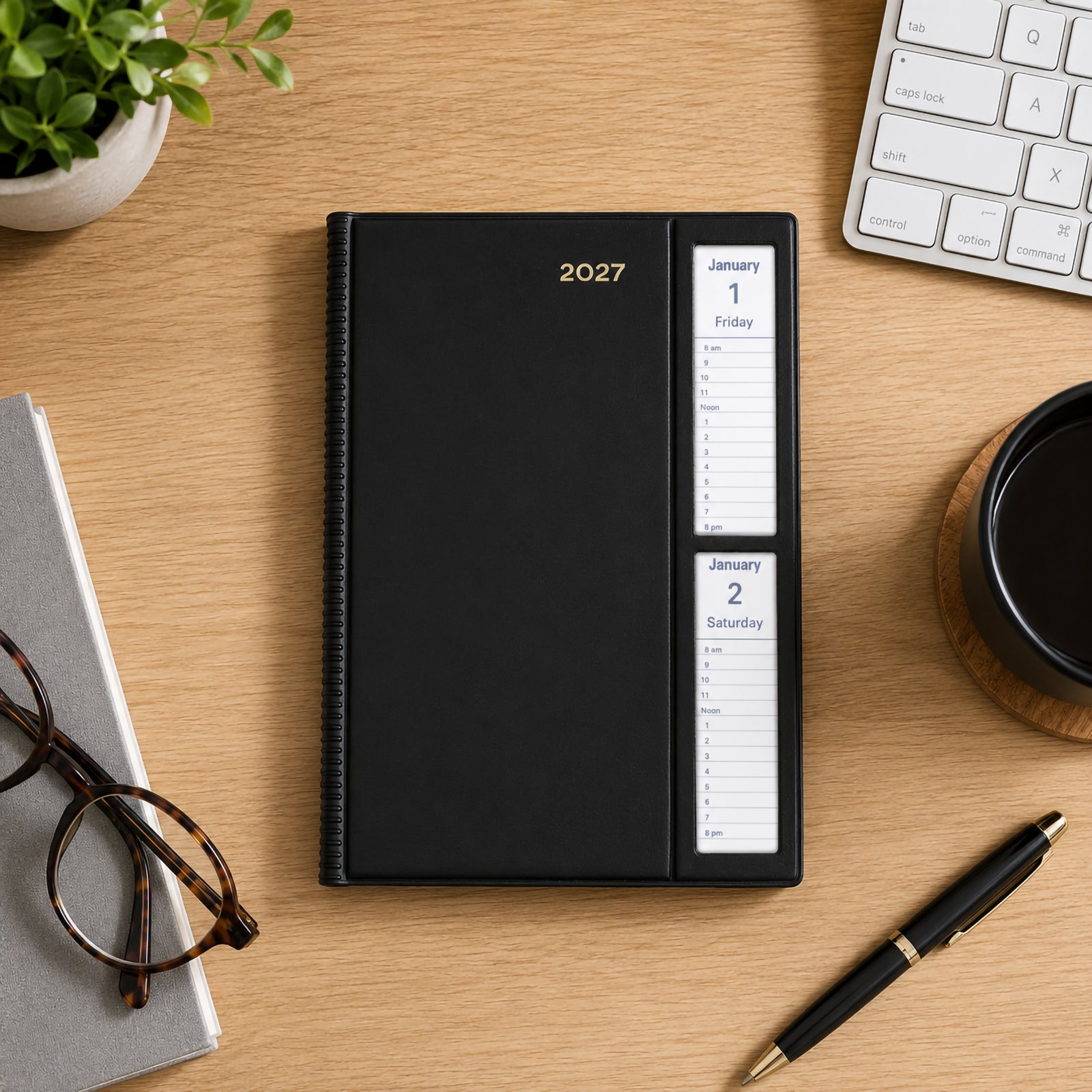 Top view of the Collins Belmont 2027 A5 Windowfaced Black Diary positioned on a timber desk beside a keyboard, notebook, glasses, coffee cup and pen. The distinctive windowfaced cover clearly displays the current day's schedule for quick reference.