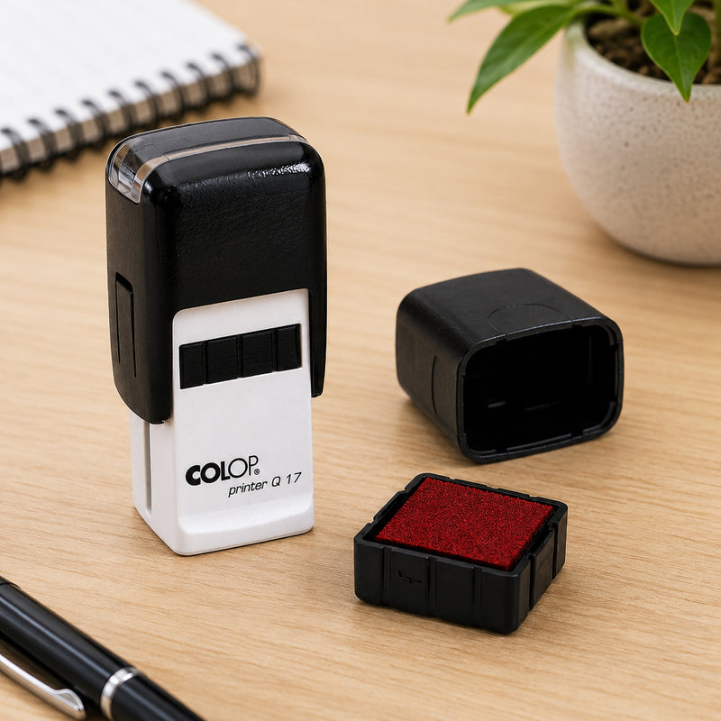 Colop Printer Q17 self inking stamp displayed on a timber office desk with the protective cover removed beside the genuine Colop Spare Pad E/Q17 Red replacement pad, demonstrating compatibility and simple replacement in a professional workspace.