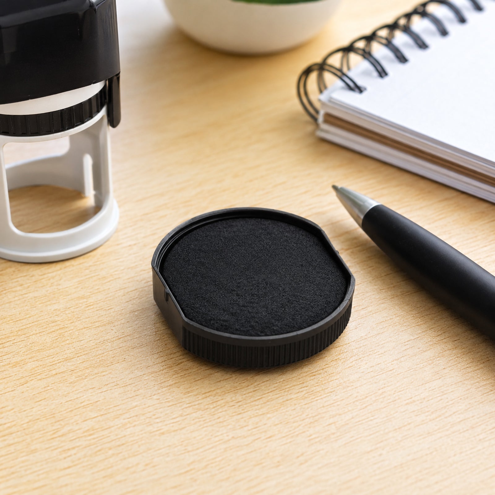 Detailed angled view of the genuine Colop Spare Pad E/R24 Black resting on a clean wooden desktop beside a notebook and pen, showcasing the textured black ink surface and durable replacement pad housing.