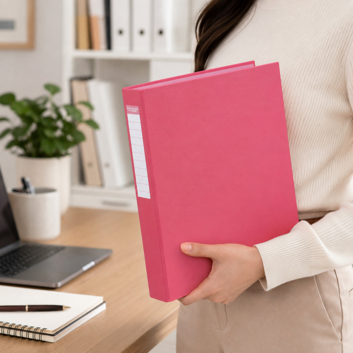 Illustrative scene from our earlier listing: a person holding a pink A4 binder against their side in a home office