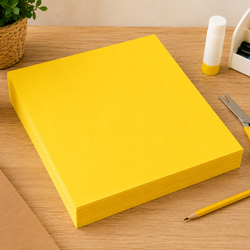Stack of lemon yellow A3 coloured board sheets neatly arranged on a wooden desk beside craft supplies including scissors, glue and pencils. The image highlights the board's consistent colour, durable 200gsm construction and suitability for bulk classroom use, displays and creative projects.