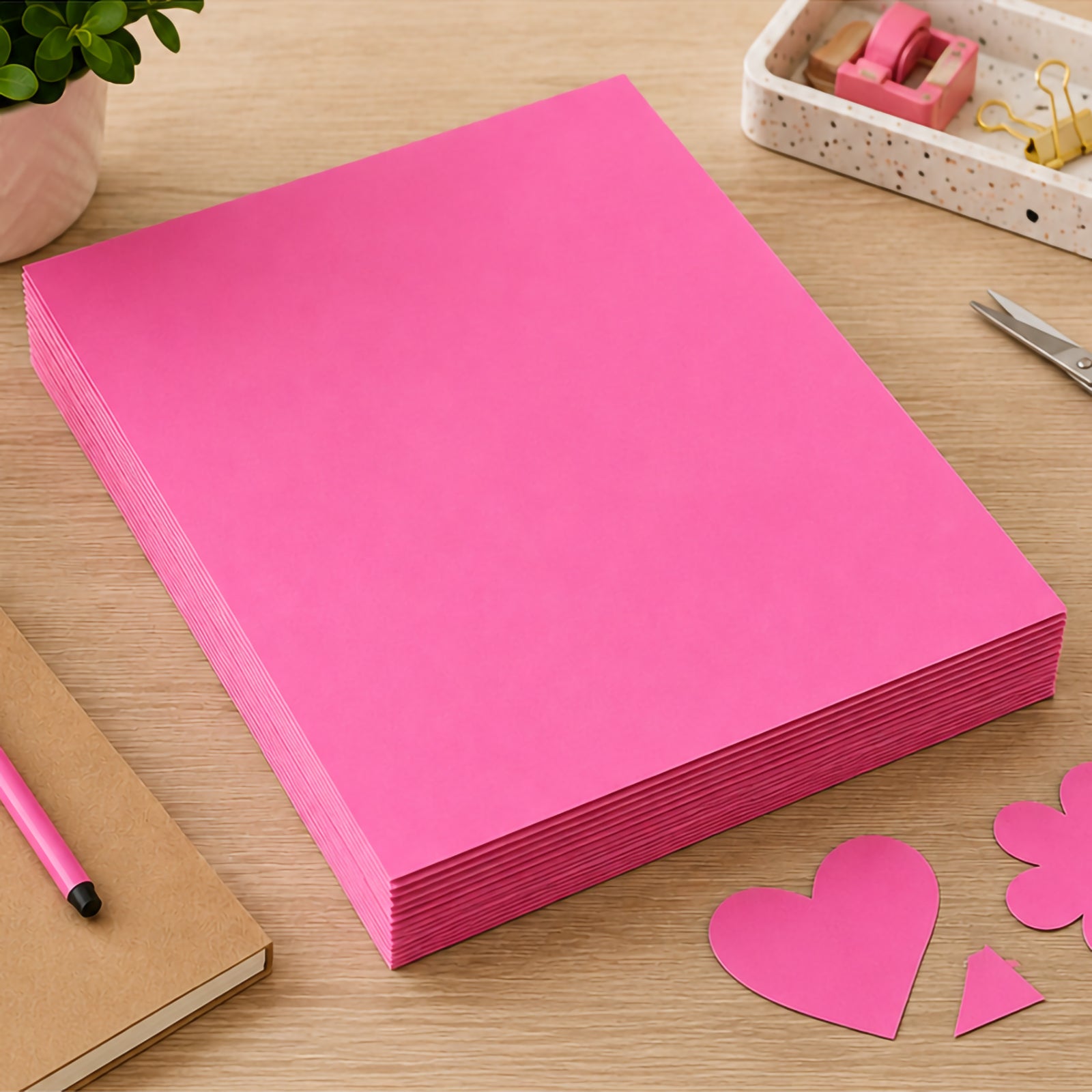 Stack of A3 pink coloured board sheets arranged neatly on a wooden desk surrounded by stationery, notebooks and craft cut outs. The image showcases the board's smooth finish, consistent colour and durable 200gsm construction for school and creative applications.