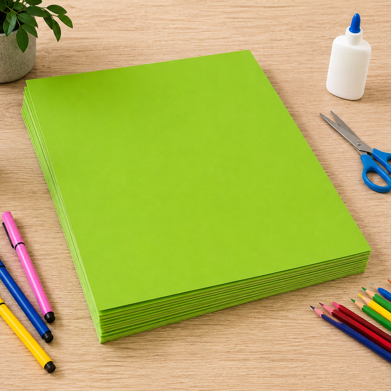 Stack of vibrant fluro green 250gsm project boards neatly arranged on a wooden craft table. Surrounded by coloured pencils, markers, scissors and glue, the image highlights the board's thickness, durability and suitability for school projects, creative displays, signage and arts and crafts applications.