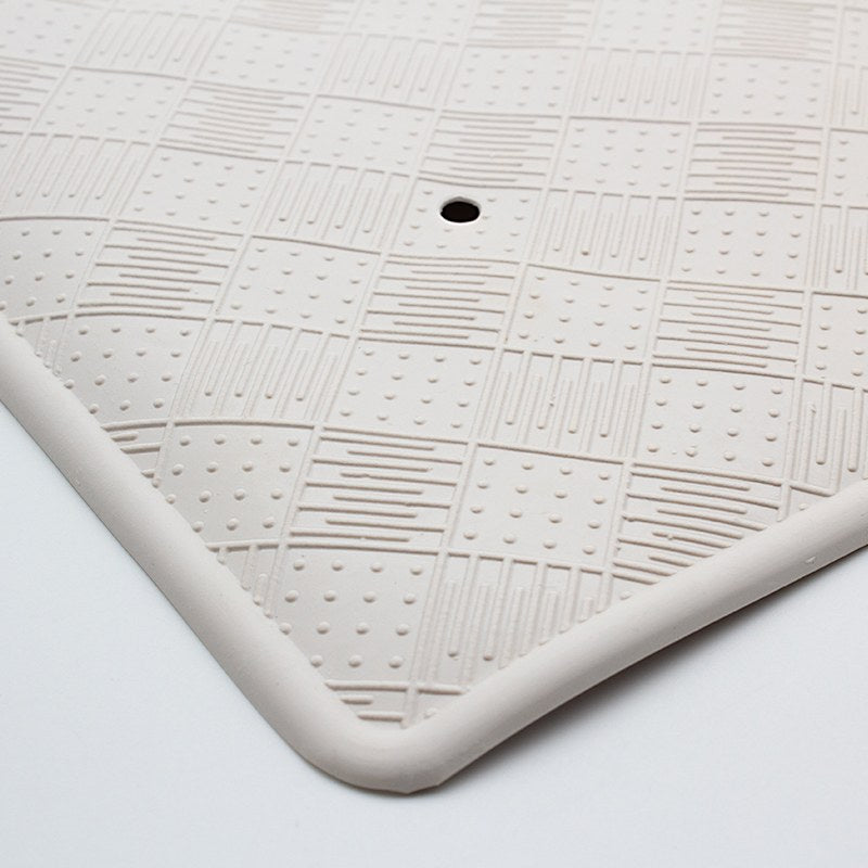 Close-up of a corner of the large rubber bath mat, the rounded raised rim and checkerboard texture around a drain hole