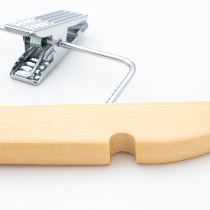 Close view of a chrome clip with its spring and ridged jaw on the wire bar, above a notched light wood shoulder end