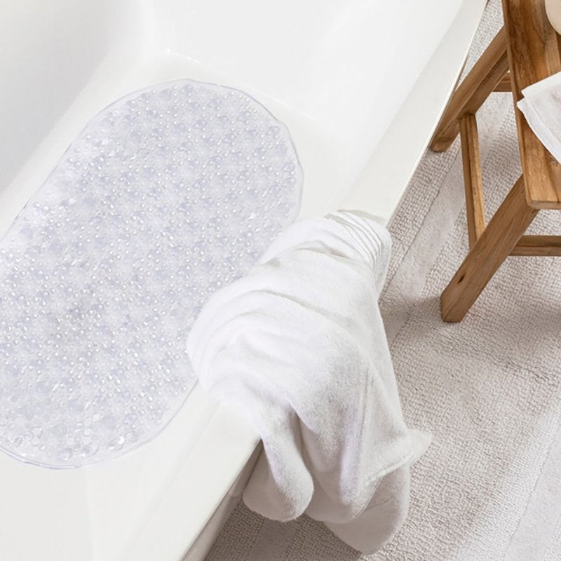 The clear Compass bath mat laid in the base of a white bathtub with a folded white towel draped over the edge of the bath