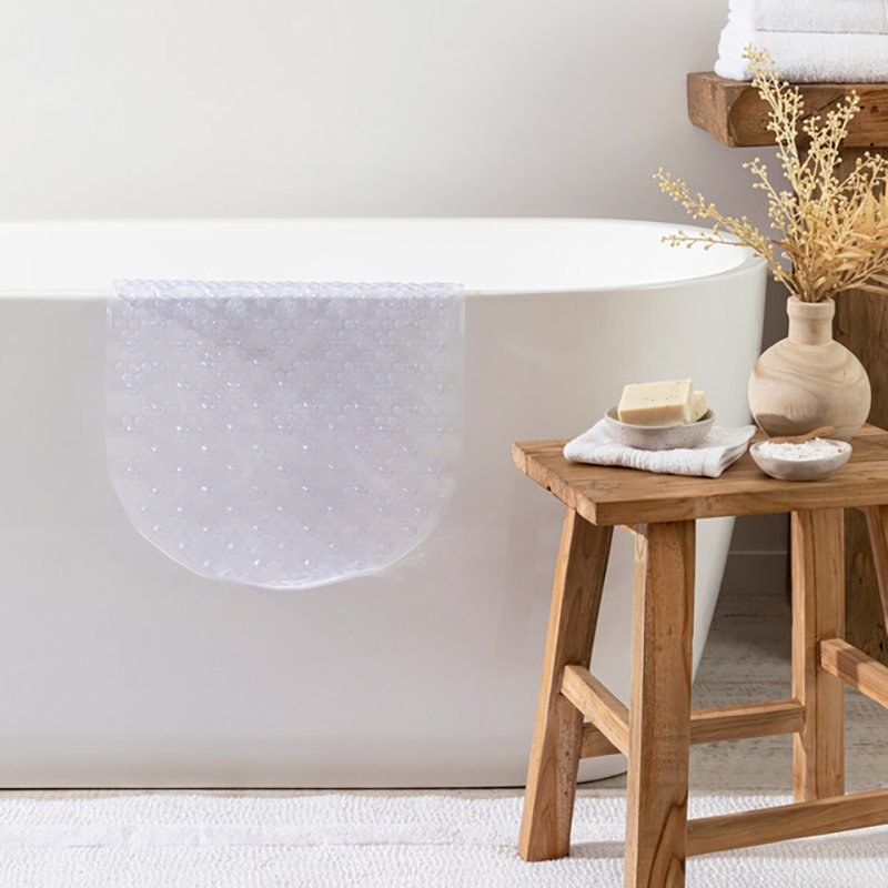 Transparent Compass bath mat inside a white freestanding bath, beside a timber stool holding soap and a small vase