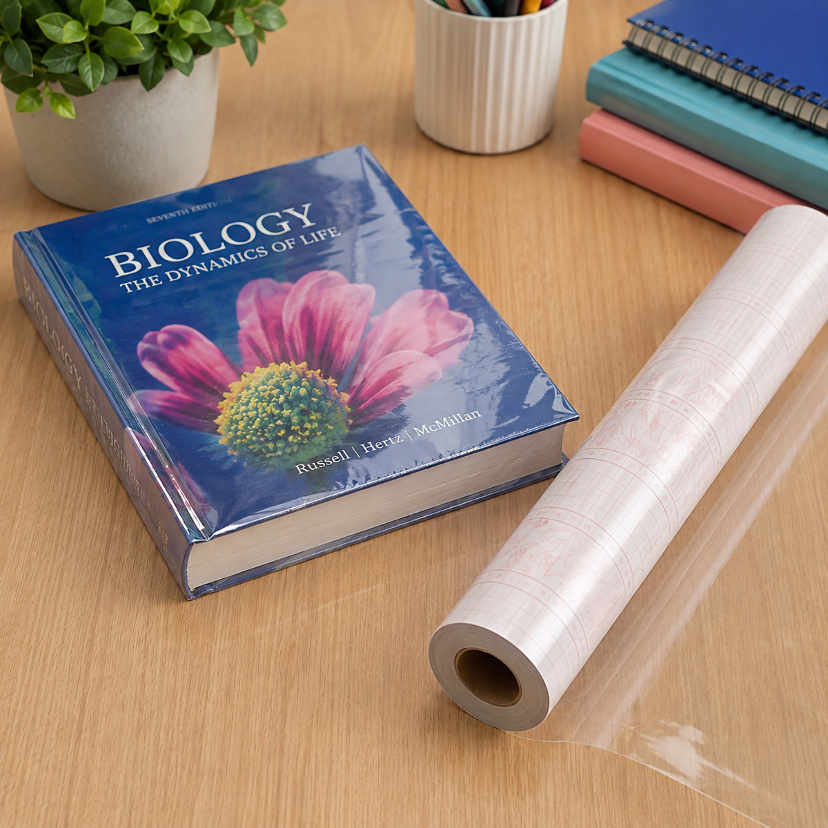 Close up lifestyle image of a biology textbook fully wrapped with ConTact Premium Clear Gloss Book Covering Film beside the 375mm x 15m roll. The glossy finish highlights the protected cover while demonstrating the film's clarity and professional appearance.