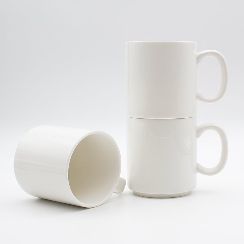 Two white stackable mugs stacked one on the other beside a third mug lying on its side