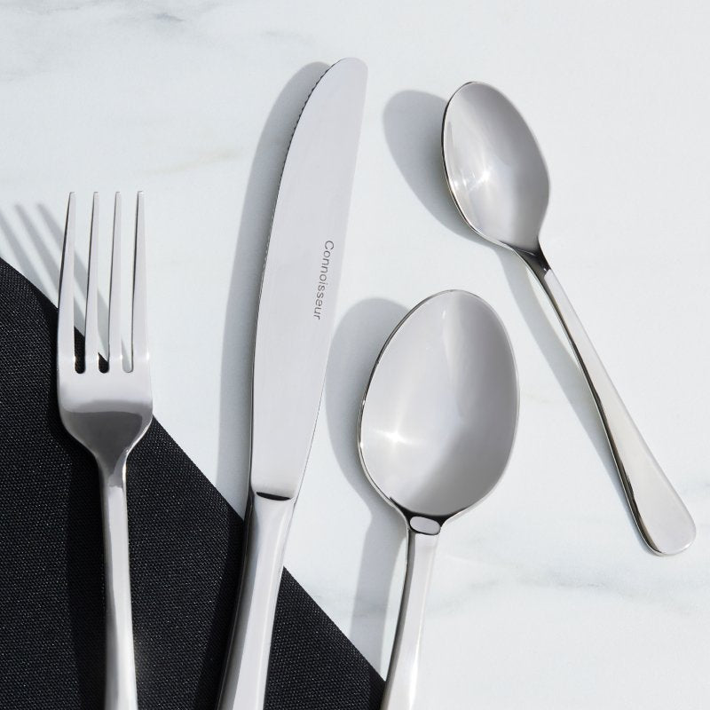 Auberge fork, knife, dessert spoon and teaspoon laid on white marble with a black napkin, the knife blade marked Connoisseur