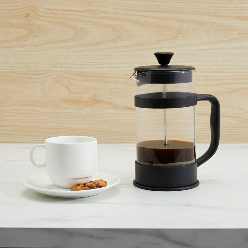 Connoisseur coffee plunger filled with coffee on a marble bench next to a white cup and saucer and biscuits