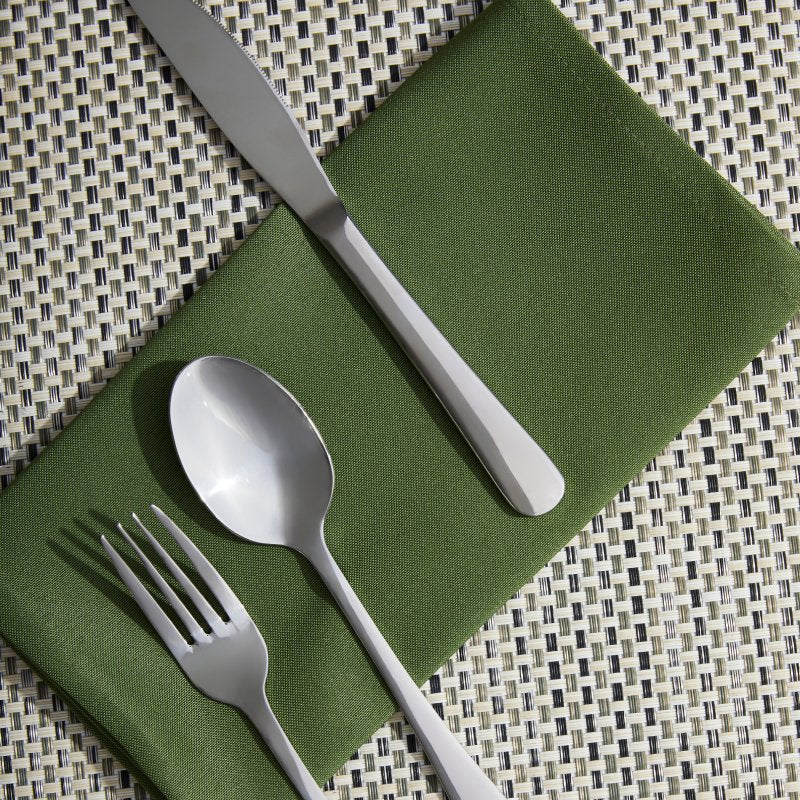 Curve knife, fork and dessert spoon laid on a green napkin over a woven black and white placemat