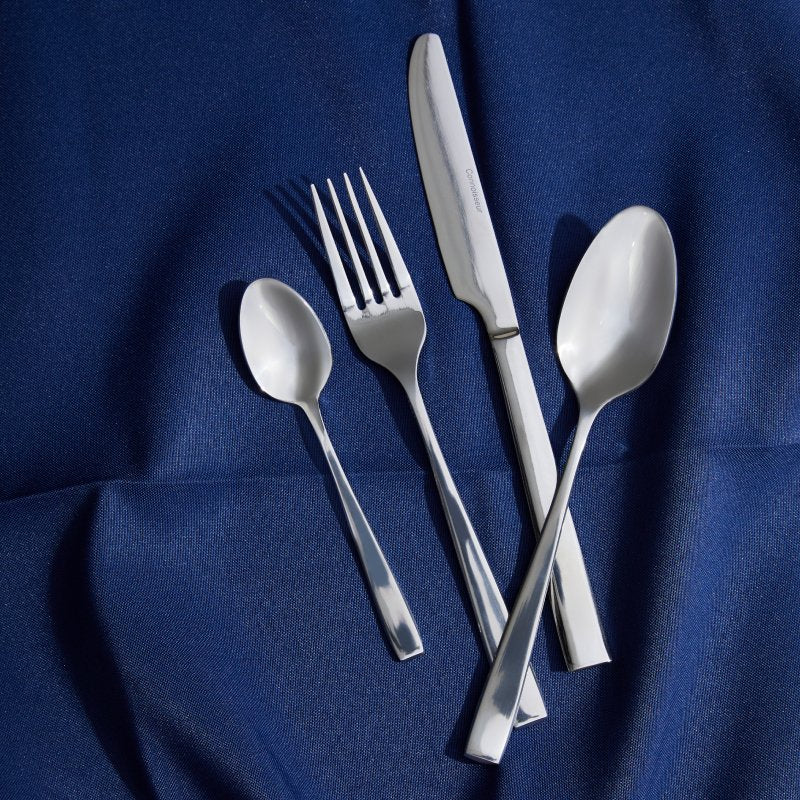 Edge knife, fork, teaspoon and dessert spoon fanned across a rich blue cloth