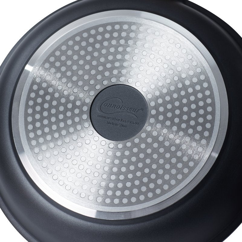 Underside of a Xylo frypan showing the polished base plate with a pattern of round dots and a Connoisseur centre badge