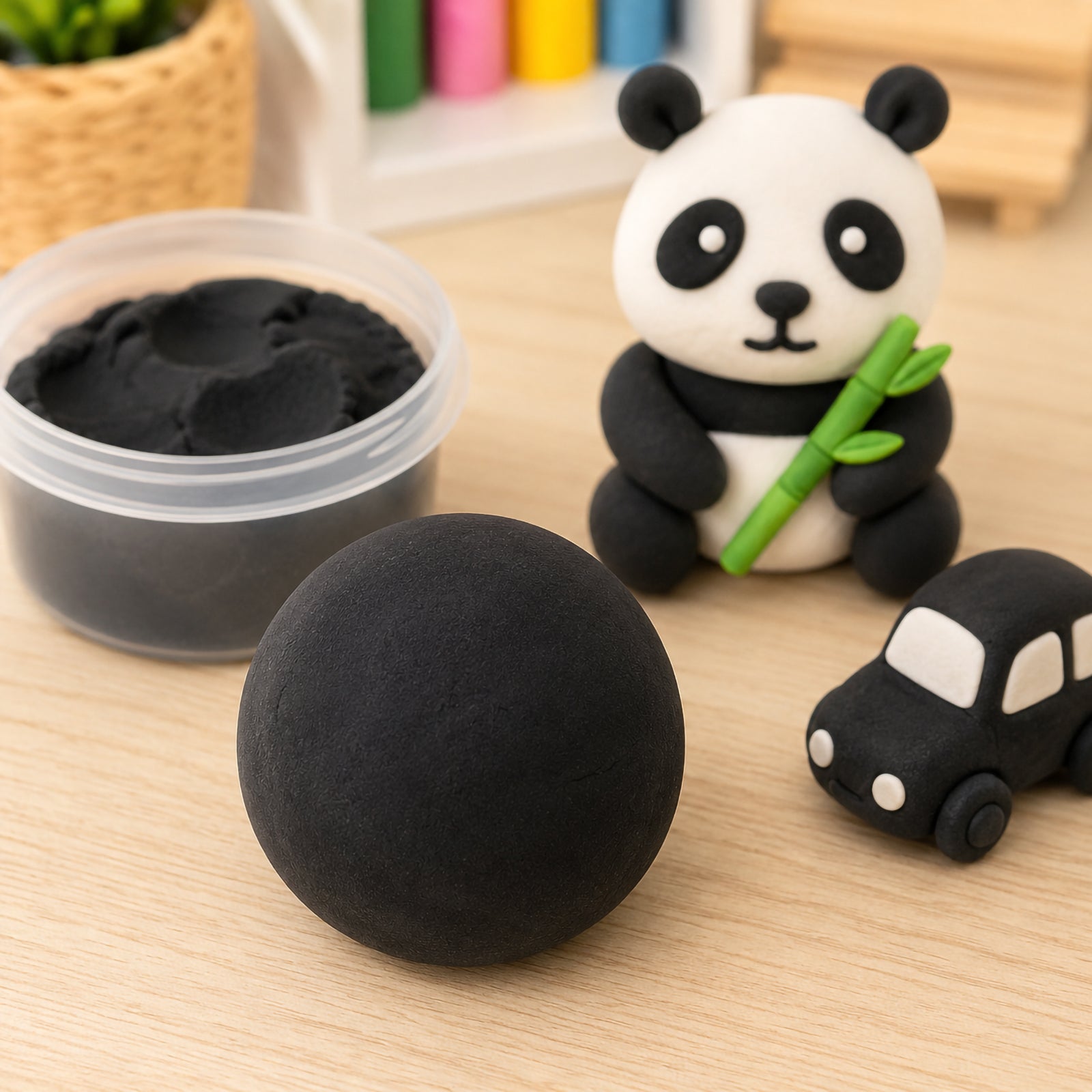 Black CreativeClay 100g displayed on a craft table with a smooth ball of black clay in the foreground. A container of clay sits beside a handmade panda figure and small model car, demonstrating the clay's smooth texture, flexibility and suitability for detailed modelling projects.