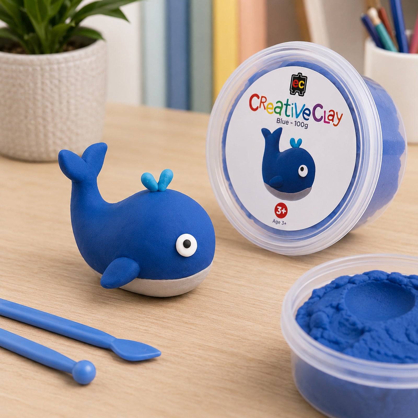 Finished whale model displayed alongside CreativeClay Blue 100g packaging and an open tub of clay. The scene showcases the product colour, lightweight modelling capability and the creative possibilities available for children, students and hobby crafters.