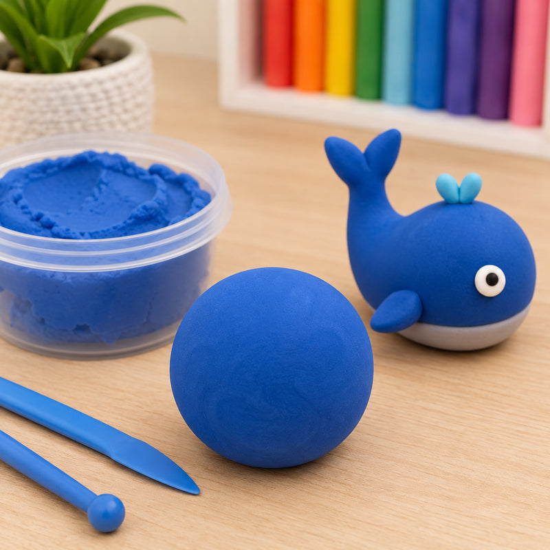 Educational Colours CreativeClay Blue 100g displayed on a wooden tabletop with a smooth blue clay ball, sculpting tools and a playful whale model. The image highlights the vibrant blue colour, soft texture and suitability for creative modelling activities in classrooms, art spaces and home craft environments.